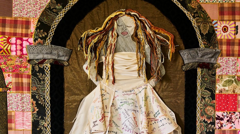 A woman wearing a white gown centres the image, with her long dress falling down, detailing embroided names